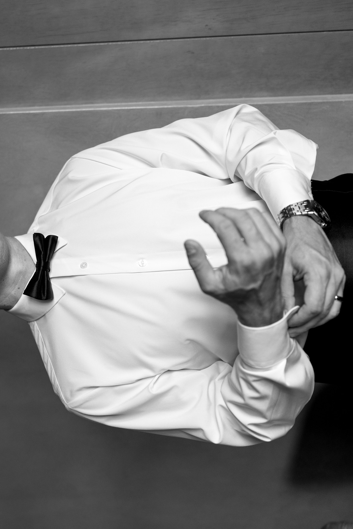 A sideways black-and-white portrait of the groom adjusting his cuff